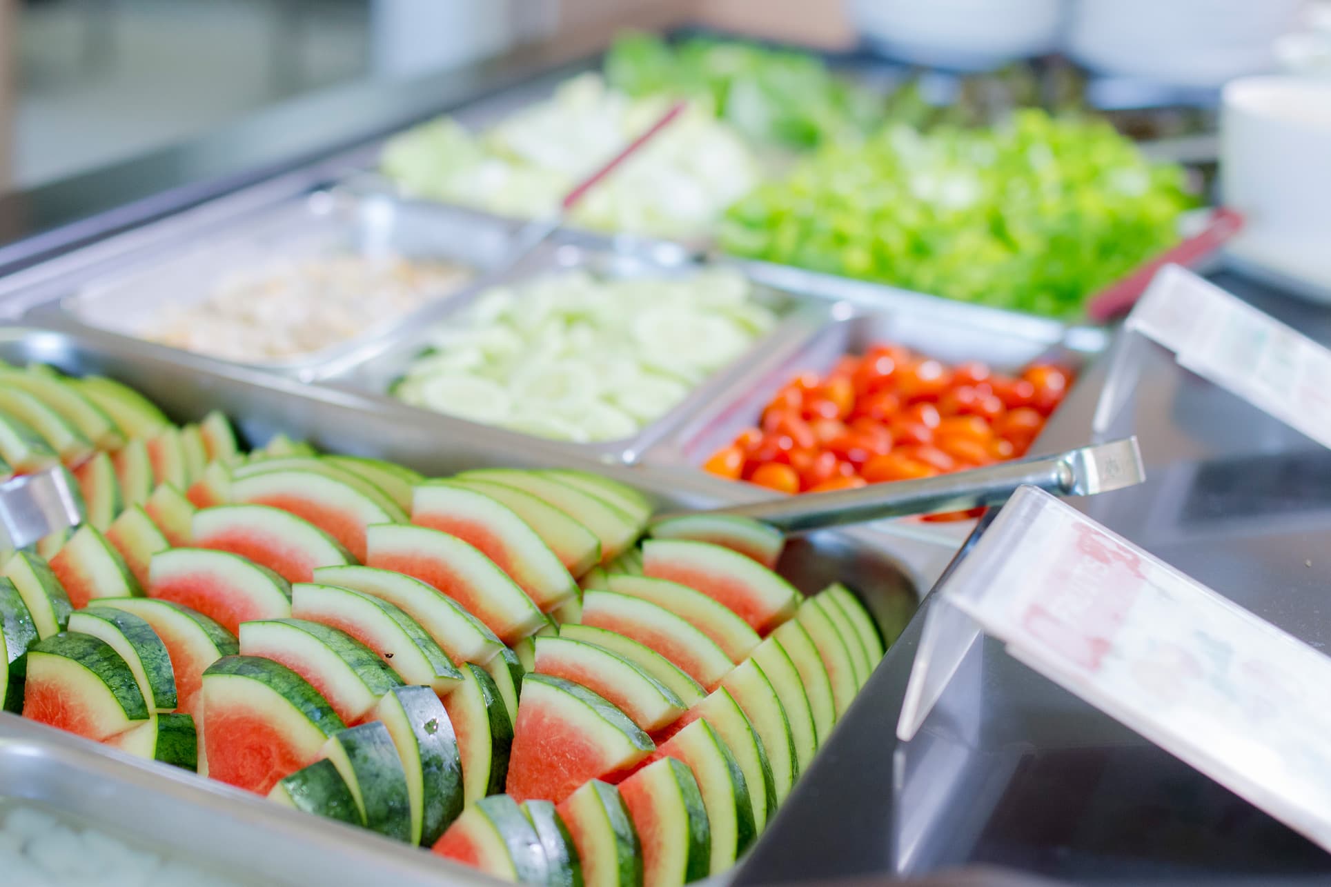 NIVA Canteen - Close-up shot of watermelon. Tomatoes, cucumber, and other salad vegetables in the background.