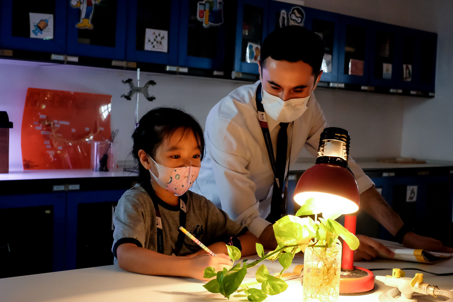 Teacher and student observing a plant under a lamp