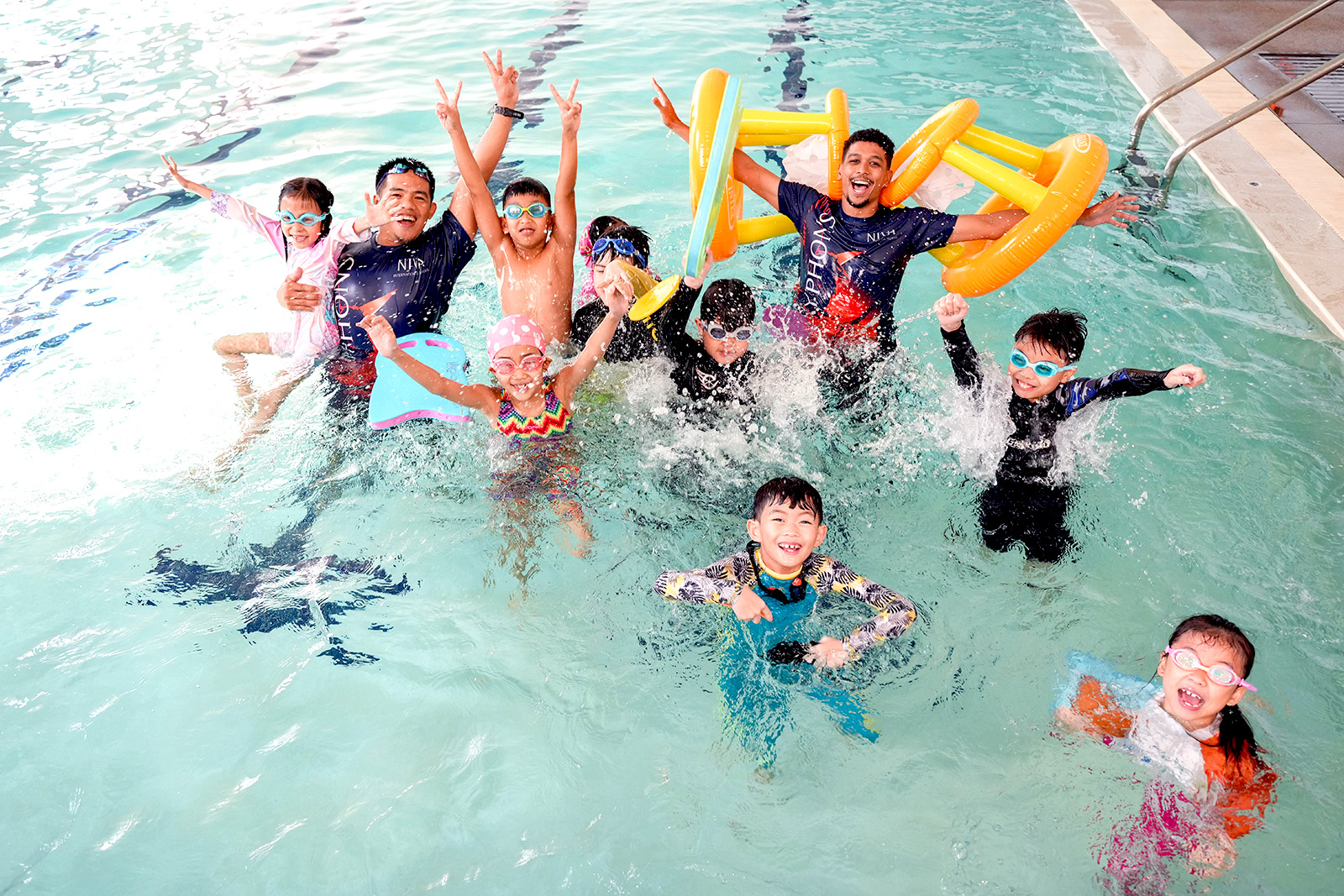 Students smiling and raising floats during swimming class