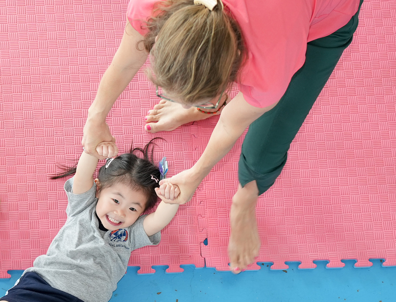 Teacher helping a kindergarten child stretch on a mat