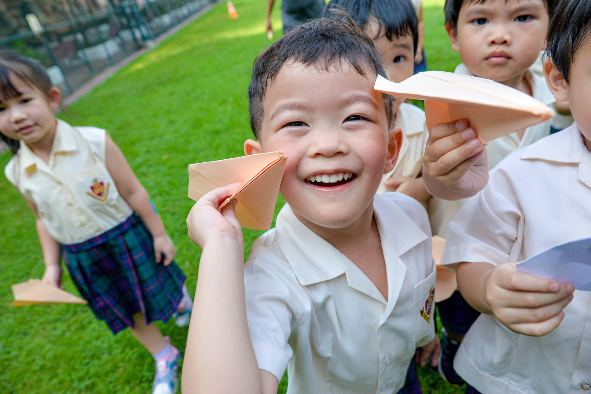 Kindergarten child showing a paper airplane on the field