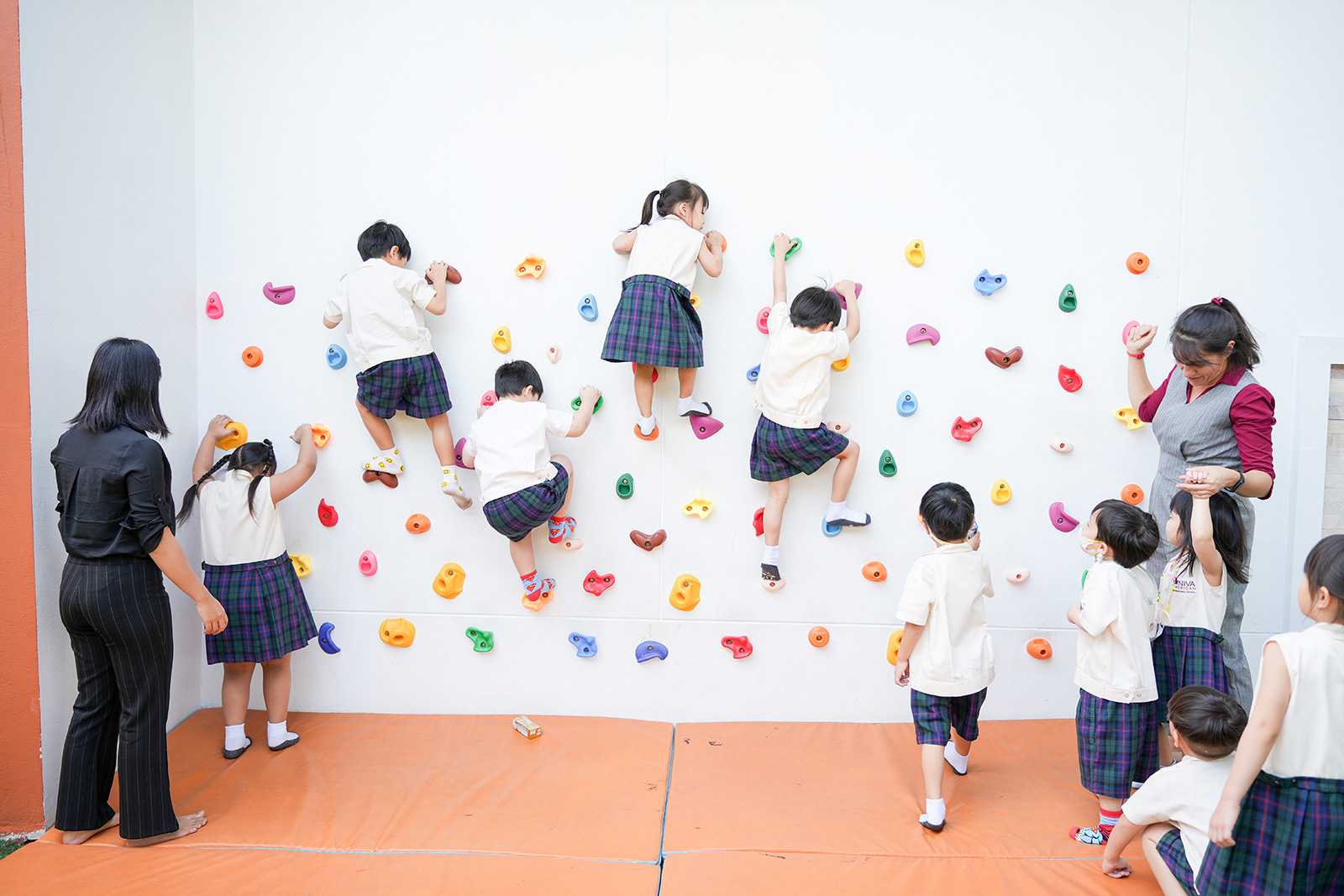 Kindergarten students climbing a wall with teachers nearby