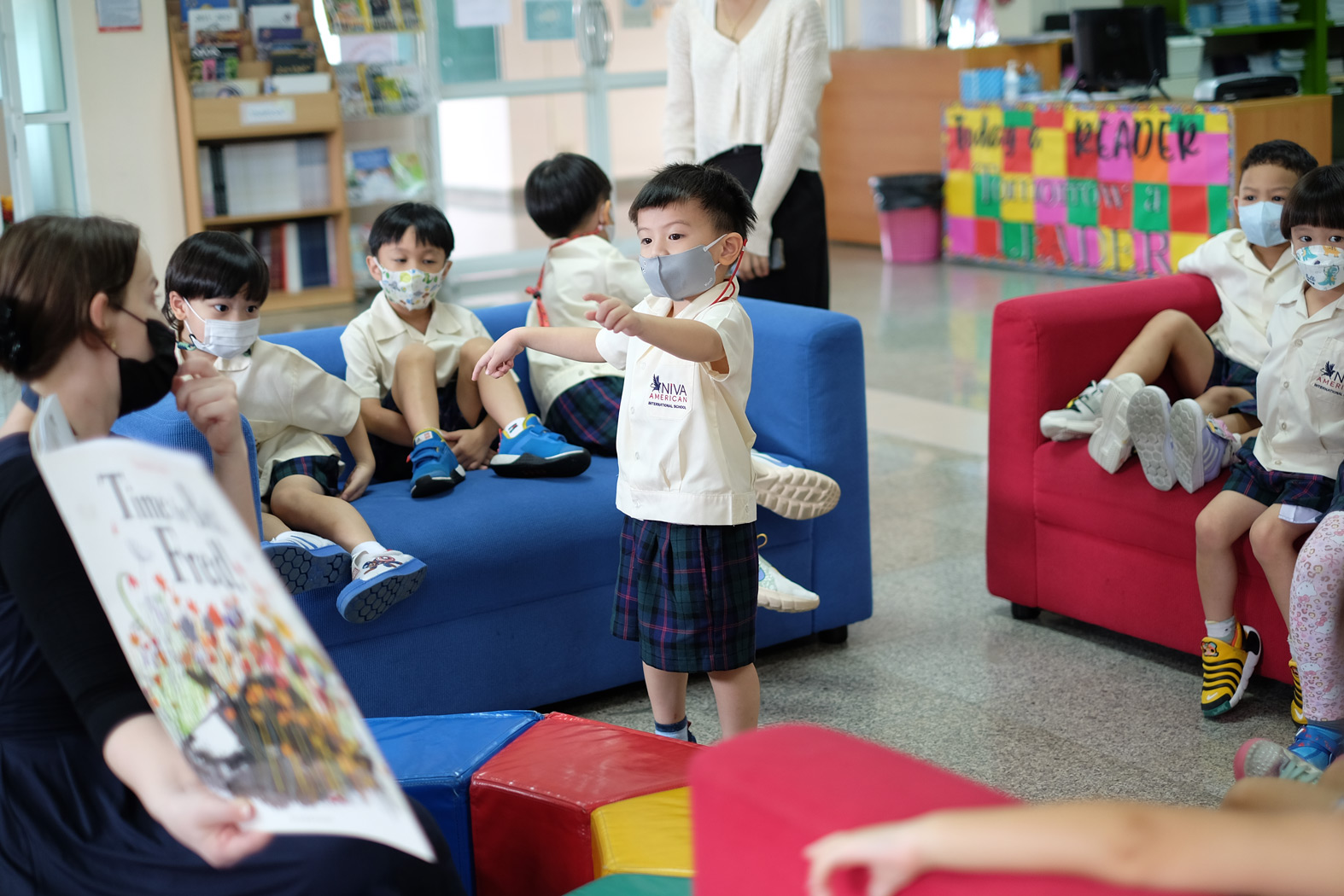 Kindergarten student showing a book to classmates in the library