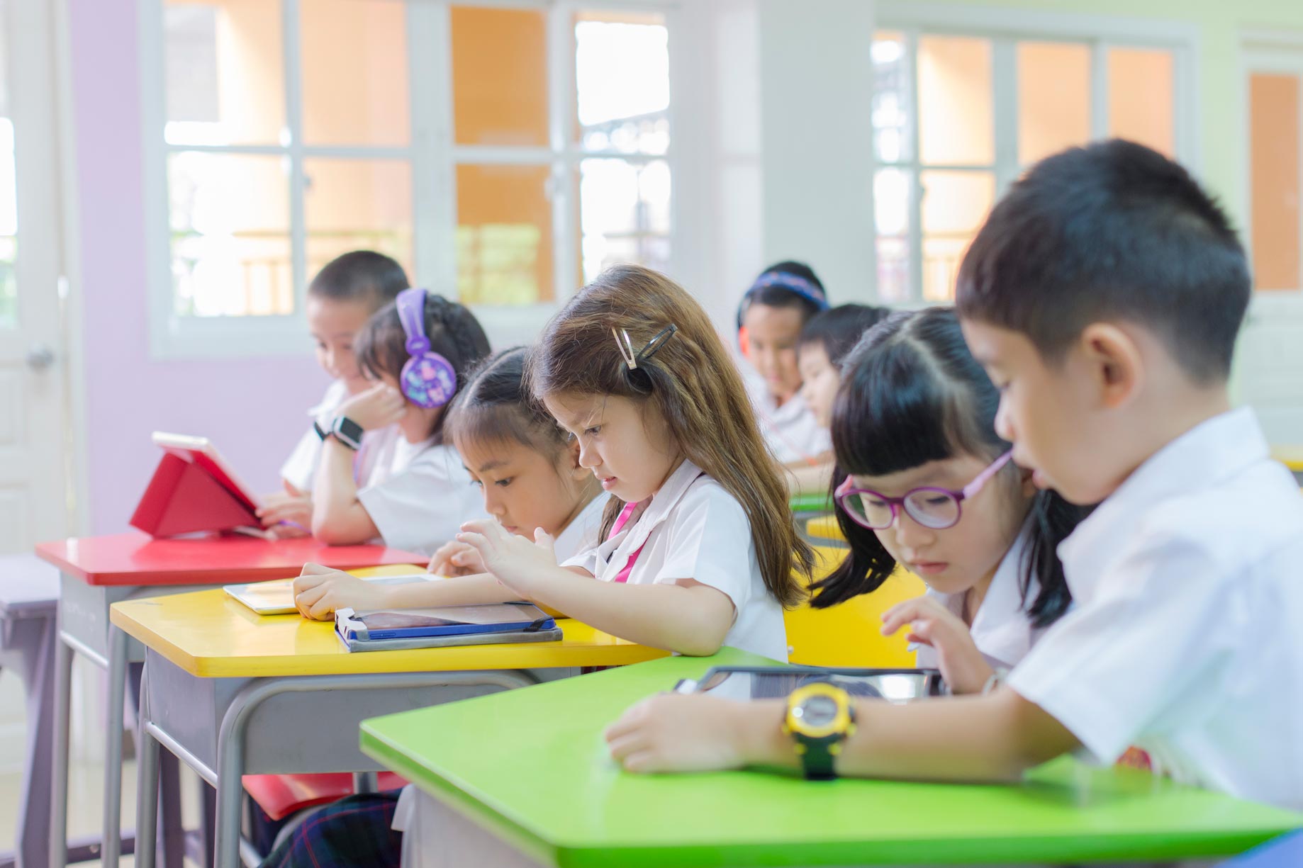 Elementary students working at colorful classroom desks