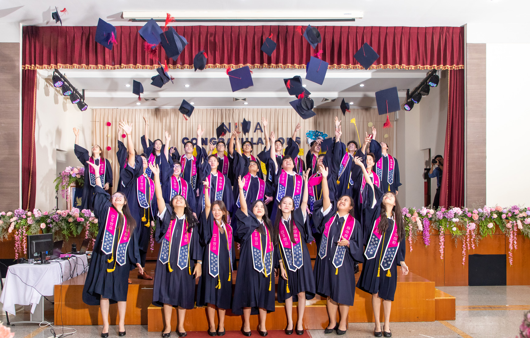 Graduates throwing their mortarboards into the air on stage