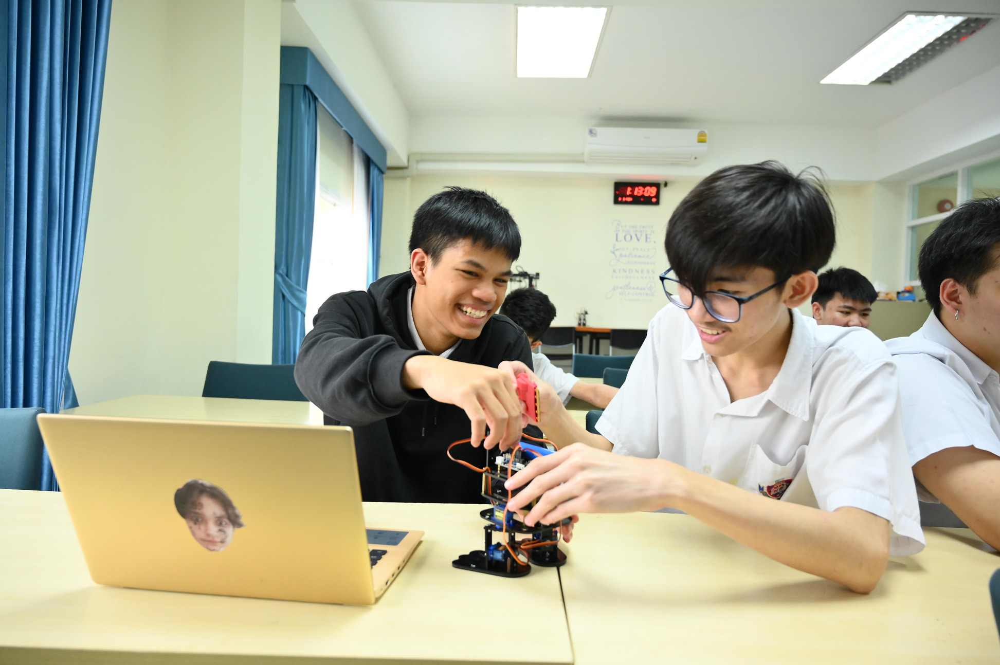 Teacher helping students build a robot beside a laptop